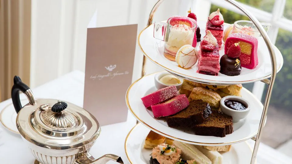 Elegant afternoon tea with assorted pastries, scones, and a teapot set on a white table by a bright window.