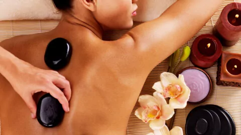Relaxing hot stone massage with candles and orchids at luxury hotel spa, offering a serene retreat experience.