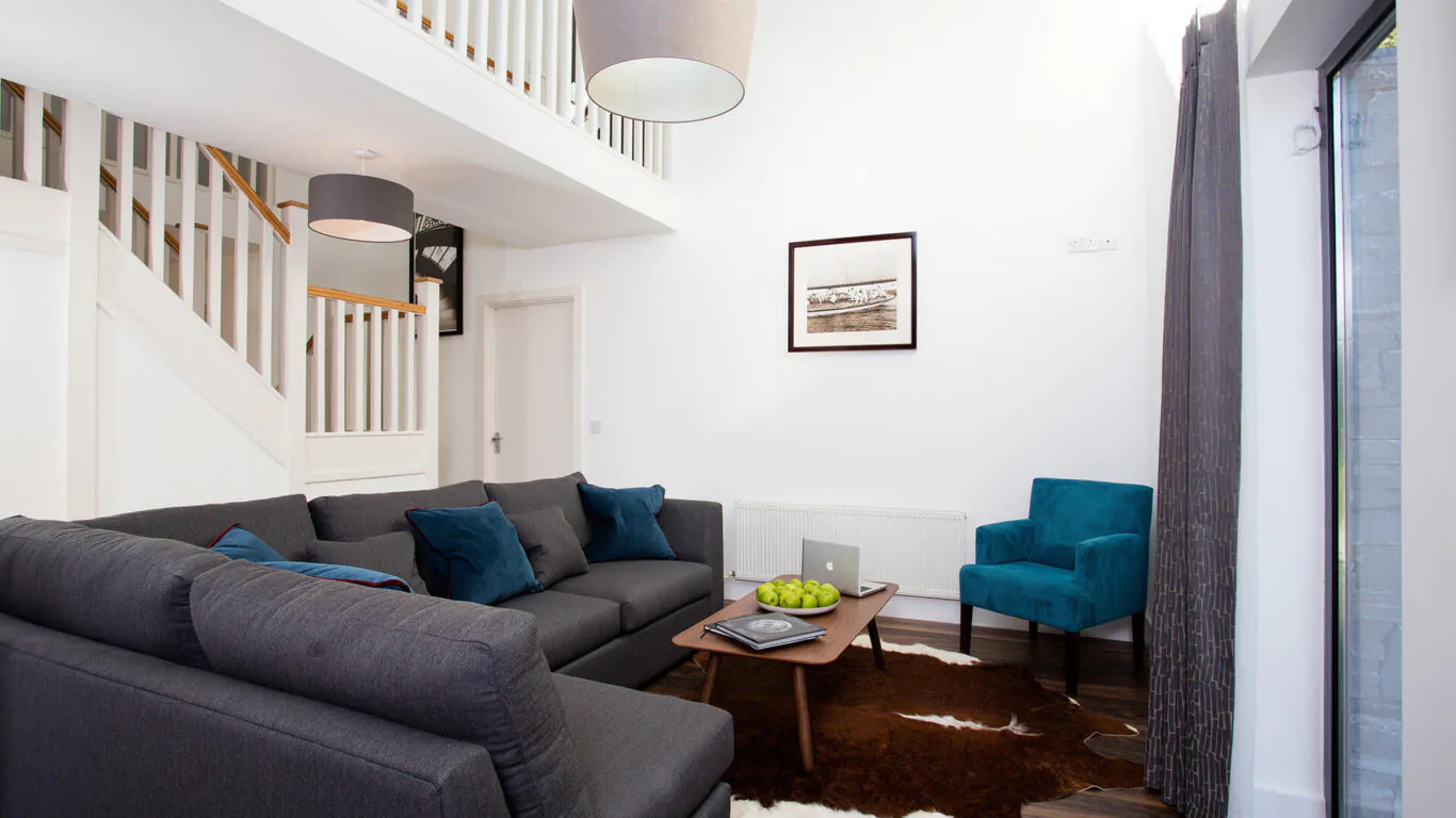 Spacious hotel living area with cosy grey sofa, teal armchair, wooden coffee table, and modern décor, perfect for relaxing.