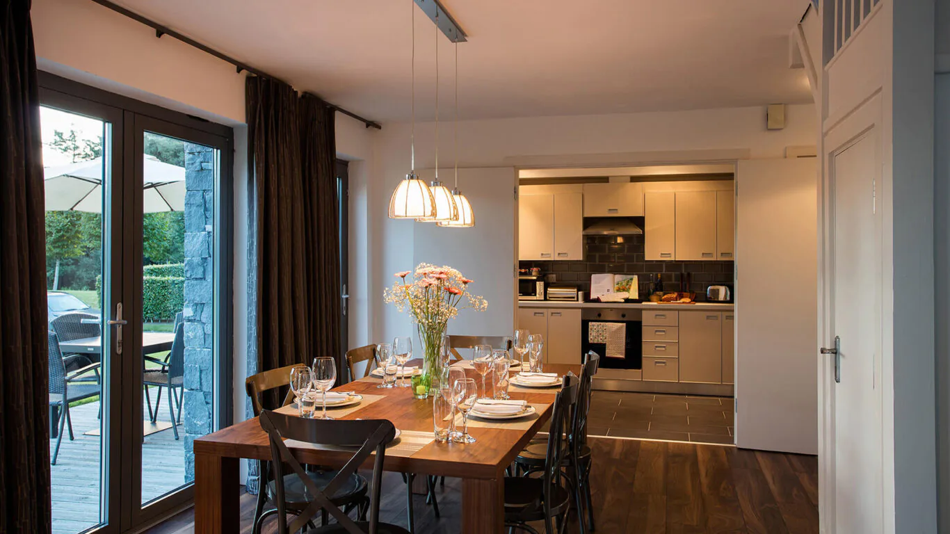 Cosy dining room with elegant table setting, modern kitchen, garden view from glass doors, ideal for intimate gatherings.