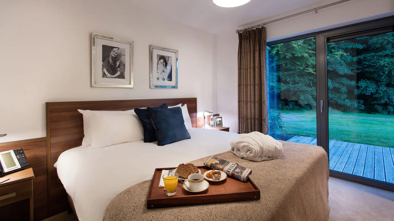Cosy hotel room with a king-size bed, plush pillows, garden view, and breakfast tray for a relaxing stay.