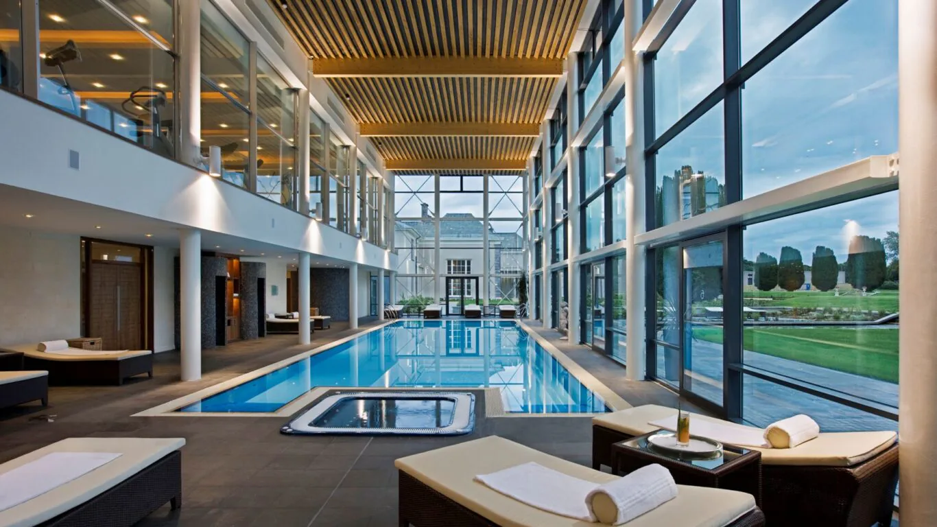 Luxurious indoor pool with sun loungers, large windows showcasing scenic gardens, ideal for a relaxing hotel stay.