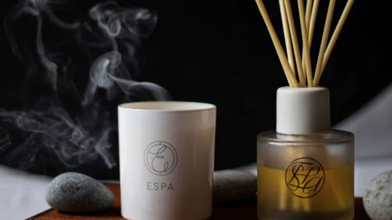 Elegant hotel spa setup with scented candle, reed diffuser, and smooth pebbles on a wooden tray, promoting relaxation.