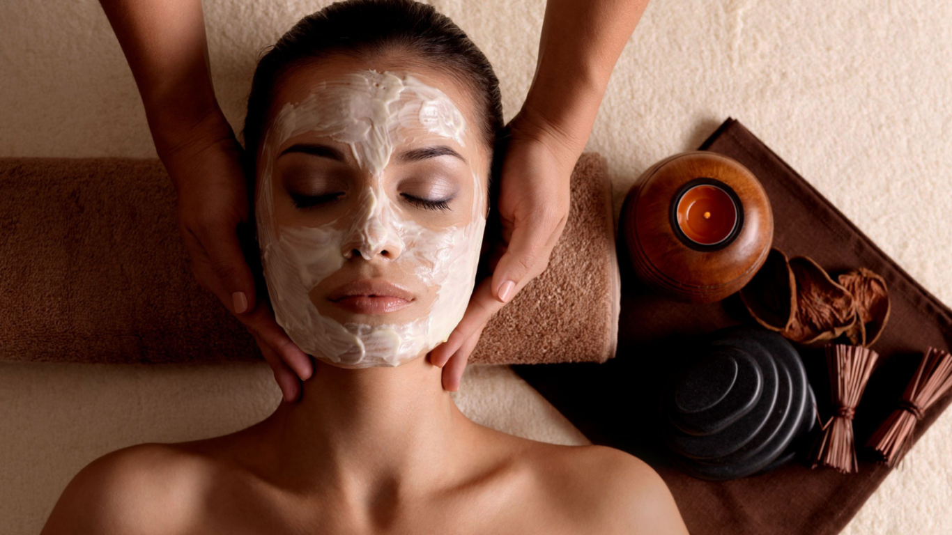 Woman enjoying a relaxing facial at spa, with aromatic candle and massage stones, offering a soothing hotel retreat.