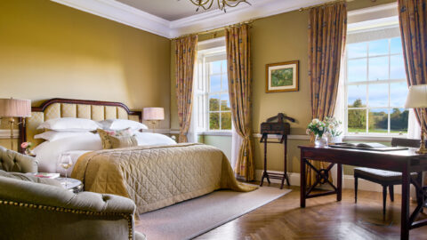 Elegant hotel room with plush bed, garden views, refined desk, cosy sofa, chic decor, inviting atmosphere.