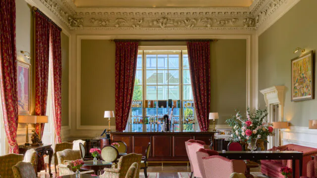 Elegant hotel lounge with plush armchairs, vibrant art, ornate decor, large windows, providing a warm, luxurious setting.
