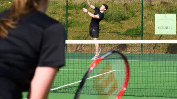 Guests enjoy a sunny tennis match on a pristine green court surrounded by lush greenery, enhancing your relaxing stay.