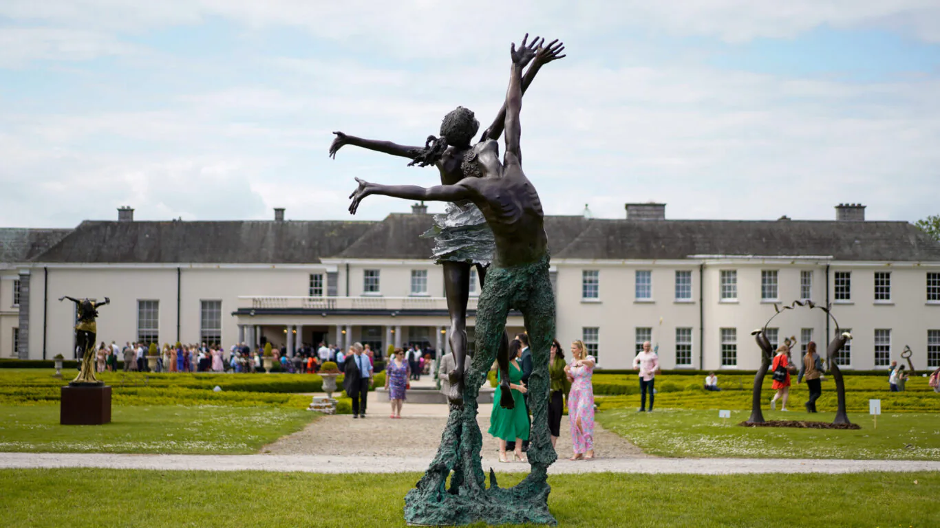 Elegant hotel garden with unique sculptures, vibrant visitors, and classic architecture under a bright blue sky.