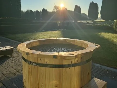 Relax in a serene garden with a wooden hot tub, lush greenery, and breathtaking sunrise views. Perfect for a peaceful retreat.