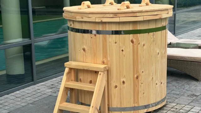 Soothing wooden hot tub at hotel patio with glass wall, offering a relaxing spa experience surrounded by lush greenery.