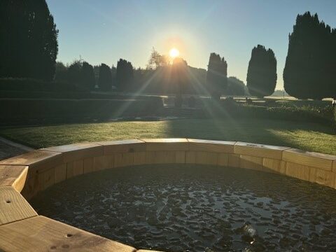 Sunrise view from hotel garden over a bubbling hot tub, surrounded by manicured lawns and tall, elegant trees.