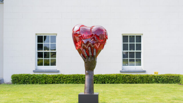 Stunning heart sculpture in lush hotel garden, framed by elegant windows, offering tranquil and artistic charm.
