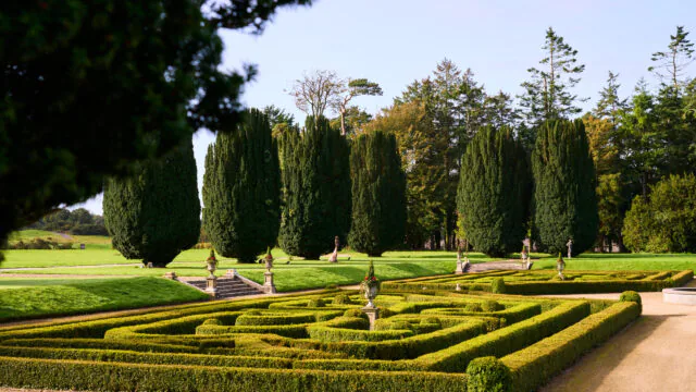 Charming hotel garden with manicured hedges, elegant statues, and majestic trees creating a serene and inviting atmosphere.