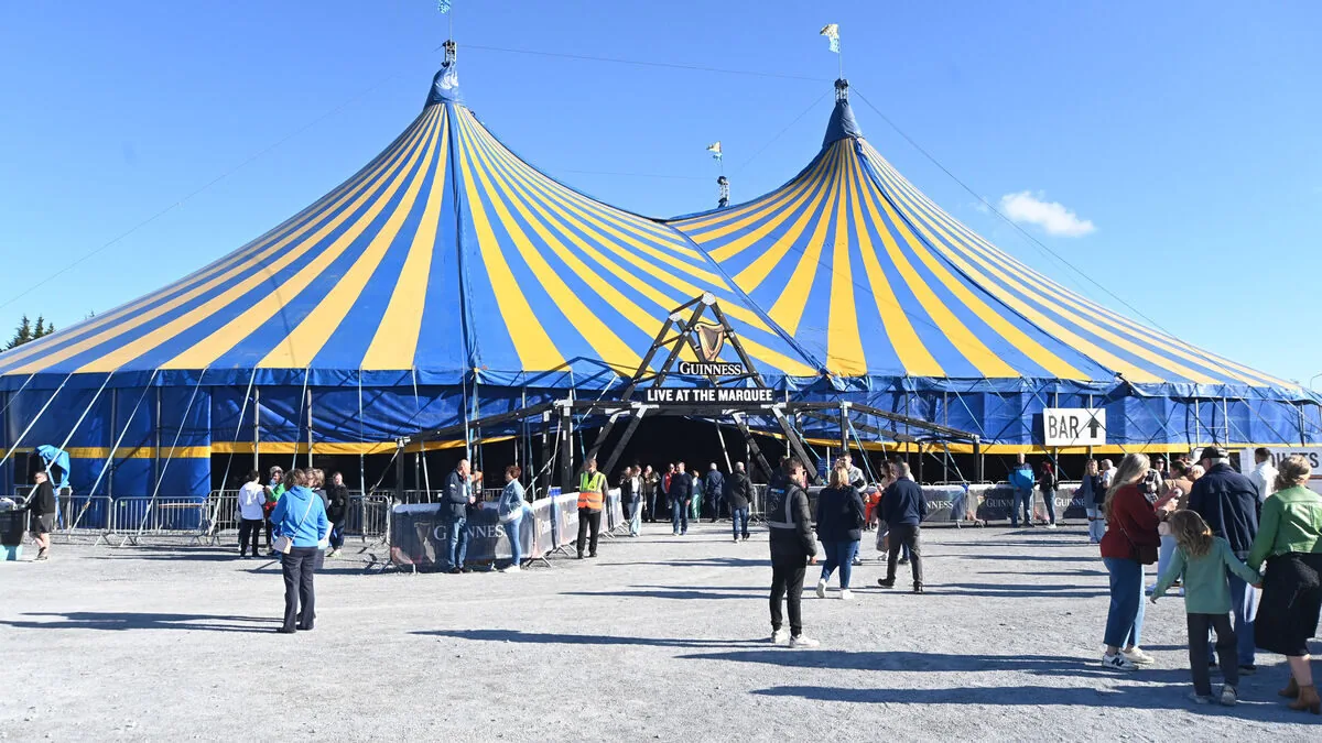 Large blue and yellow striped circus tent with people gathered outside; a sign reads