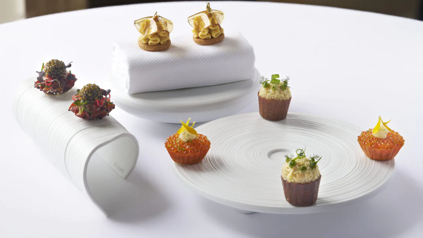 Elegant gourmet appetisers on white plates by a sunlit window, offering a luxurious dining experience at the hotel.