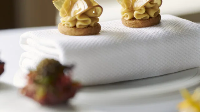 Elegant afternoon tea pastries on a crisp white napkin at a luxury hotel, with lush garden view in background.