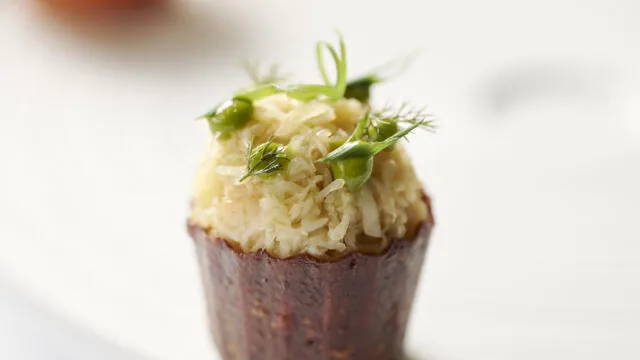 Gourmet canap&eacute; with delicate garnish on elegant white plate, showcasing luxury hotel dining experience.