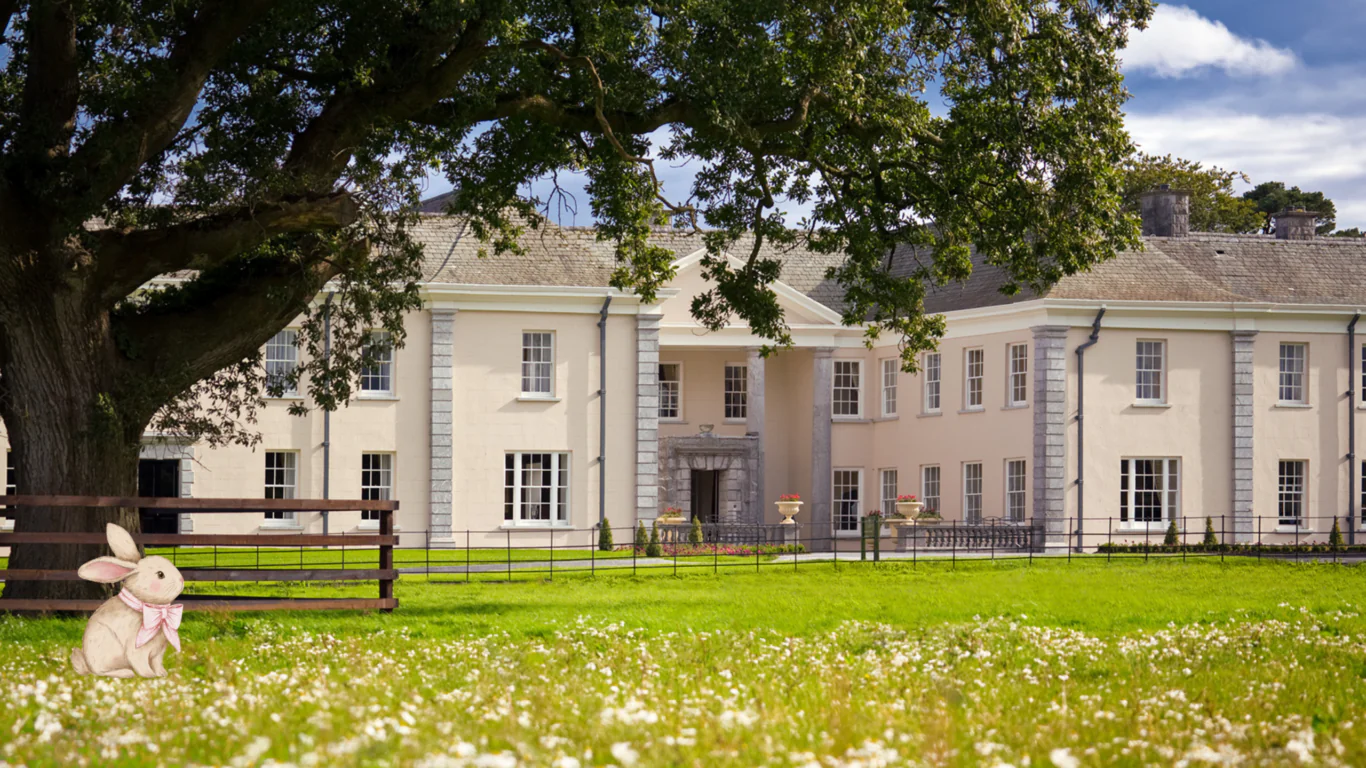 Elegant country hotel with grand entrance, lush green lawn, charming garden, and vibrant flowers under a picturesque sky.