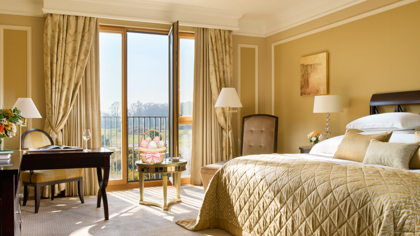 Elegant hotel room with king-sized bed, balcony view, chic decor, cosy seating, natural light, and welcoming atmosphere.