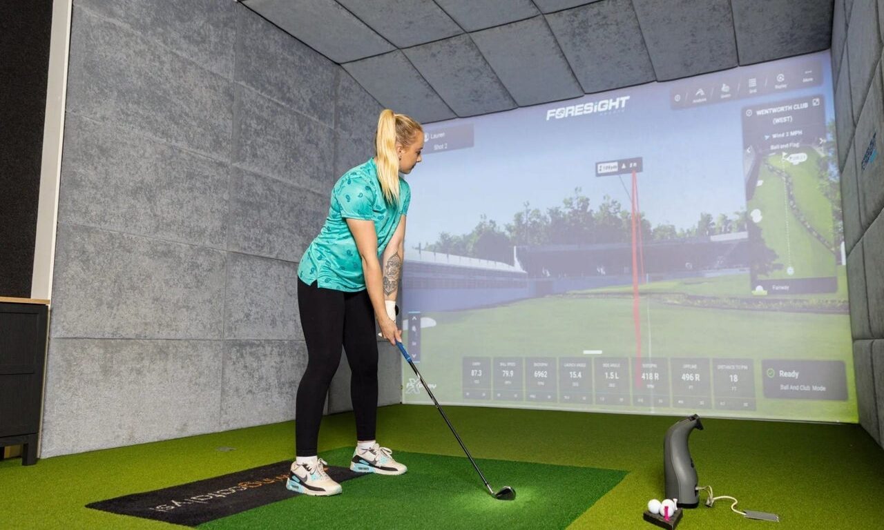 Guest enjoying indoor golf simulator at hotel with high-tech screen and golf equipment on artificial turf.