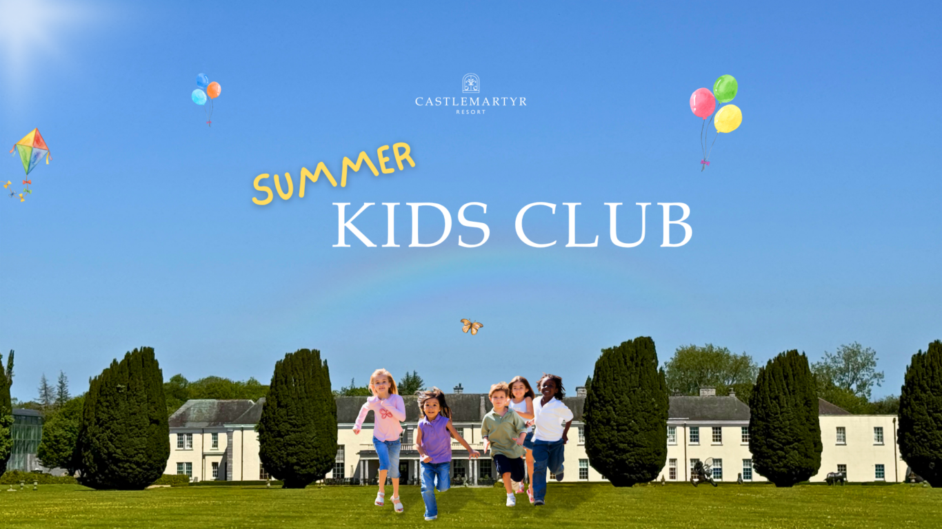 Children playing on lush lawn in front of Castlemartyr Resort's Kid's Club, with balloons and kites in a bright summer sky.