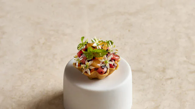 Exquisite gourmet tart with fruit and edible flowers on a marble background, showcasing luxury hotel dining experience.