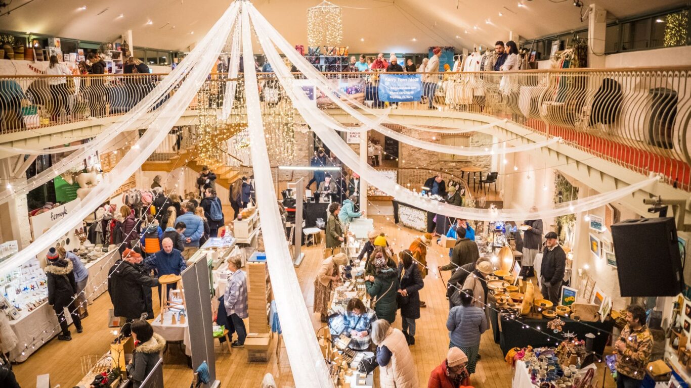 Guests explore a lively indoor market with festive decor, local crafts, and friendly vendors in a beautifully lit hotel atrium.